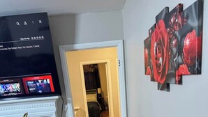A room with a desk, a computer monitor displaying a streaming service, a black leather chair, and a hallway leading to another room. - 3BR King Beds | 85” TV | 4min to A&T & Downtown (Greensboro)