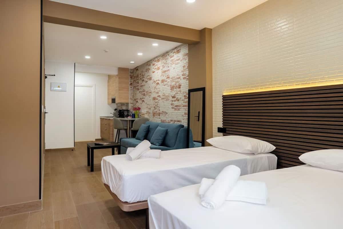A hotel room with two beds, a sofa, a small table, and a kitchenette in the background.