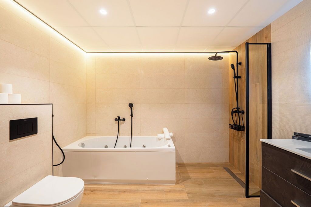 Een moderne badkamer met een bad, douche en toilet.