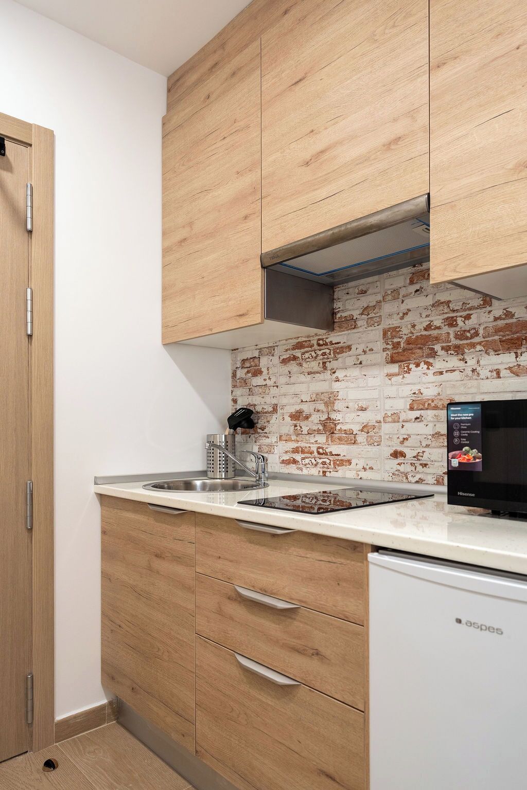 Una cocina compacta con armarios de madera, un lavamanos de acero inoxidable y un lavavajillas.