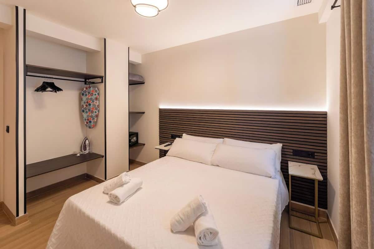 A hotel room with a neatly made bed, a bedside table, a nightstand, and a built-in wardrobe with a hanging rack.