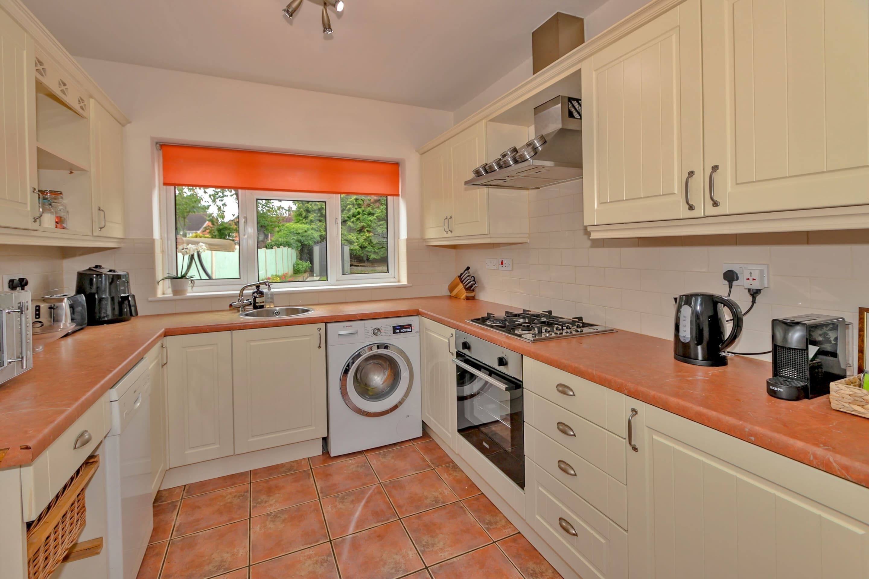 A compact kitchen with white cabinets, a washing machine, an oven, and a coffee maker.