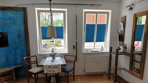 Una habitación con suelo de madera, una mesa con sillas, un radiador y una ventana con contraventanas azules.