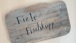 Una placa de madera con el texto 'Fiete Fischkopf' colocada en una pared.