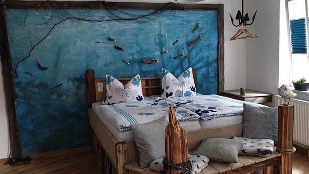 Un dormitorio rústico con una cama grande, cabecera de madera y un mural de peces en la pared.