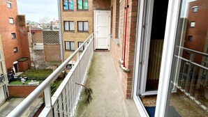A narrow balcony with a concrete floor, a white door, and a glass door leading to a room. - Apartment 700 Meters From Baldus Beach (Koksijde)