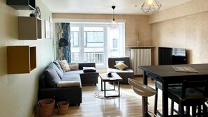 A modern living room with a sofa, a dining table, and a kitchen area. - Apartment 700 Meters From Baldus Beach (Koksijde)