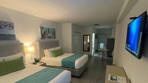 Habitación de hotel con dos camas, un escritorio, televisión y un pasillo que conduce a un baño.