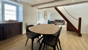 A dining area with a wooden table and black upholstered chairs, a window with a view, and a staircase leading to an upper level. - Ty Camelia-Draps included-4p-Wifi-Enclosed garden (QUIBERON)