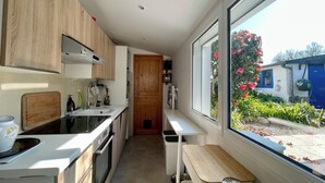 A modern kitchen with wooden cabinets, a built-in oven, a sink, and a window overlooking a garden. - Ty Camelia-Draps included-4p-Wifi-Enclosed garden (QUIBERON)