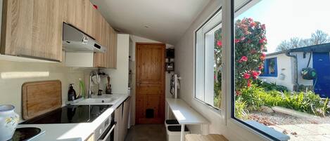A modern kitchen with wooden cabinets, a built-in oven, a sink, and a window overlooking a garden.