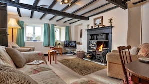 Un salón acogedor con chimenea, sofá floral, vigas de madera y televisor.