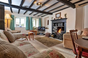 A cozy living room with a fireplace, floral sofa, wooden beams, and a television.