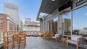 Terraza en la azotea con mobiliario de madera y amplios ventanales con vistas a la ciudad.