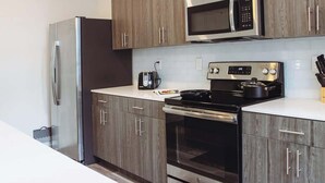 Una cocina con refrigerador de acero inoxidable, microondas, estufa y alacenas de madera.