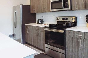 A kitchen with a stainless steel refrigerator, a microwave, a stove, and wooden cabinets.