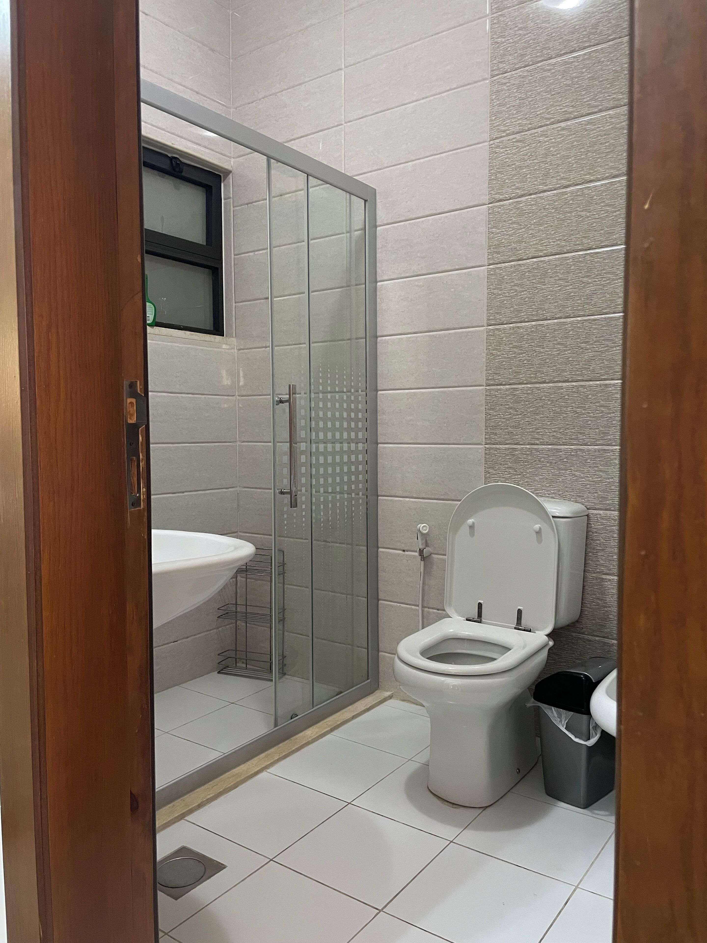 Une salle de bain avec une douche à parois de verre, un lavabo, des toilettes et une poubelle.