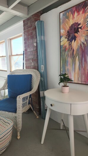 A wicker chair with a blue cushion, a white table with a pink plant, and a large floral painting on the wall. - CHARMING , NEW RENO, STUDIO APT.
MTHLY RENTAL JUNE START - 1 1/2 BLOCKS TO BEACH (Ocean Grove)