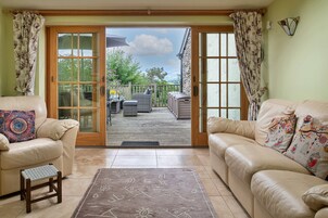 Una sala de estar con dos sofás color beige, una alfombra pequeña y vistas a un patio exterior con una mesa y sillas de madera.