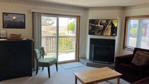 A living room with a fireplace, a green chair, a wooden table, and a dark-colored sofa. - True Ski In/Out  2 bedroom condo (Jay)