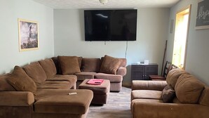A living room with a sectional sofa, ottomans, a flat-screen TV, and a wooden herringbone floor. - Welcome to Gods country lodging located in the heart of Hatfield and mcoy trails (Delbarton)