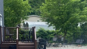 A covered outdoor area with a gravel floor, a wooden deck with stairs, and outdoor furniture. - Welcome to Gods country lodging located in the heart of Hatfield and mcoy trails (Delbarton)