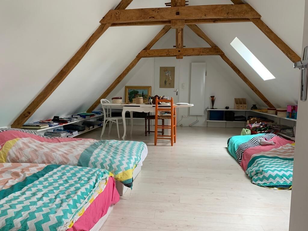 Un dormitorio abrigado en un ático con techo inclinado, un escritorio y dos camas con ropa de cama colorida.