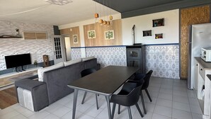 Une cuisine moderne avec un coin repas, comprenant un canapé gris, une table à manger avec des chaises et un four encastré.