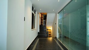 Ein moderner Flur mit einer Glaswand rechts, einer Treppe in der Mitte und einer Tür am Ende.