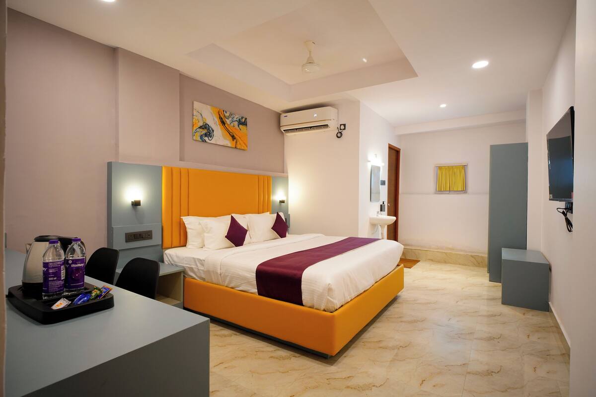 A modern hotel room with a large bed, a desk with a coffee maker, and a TV.