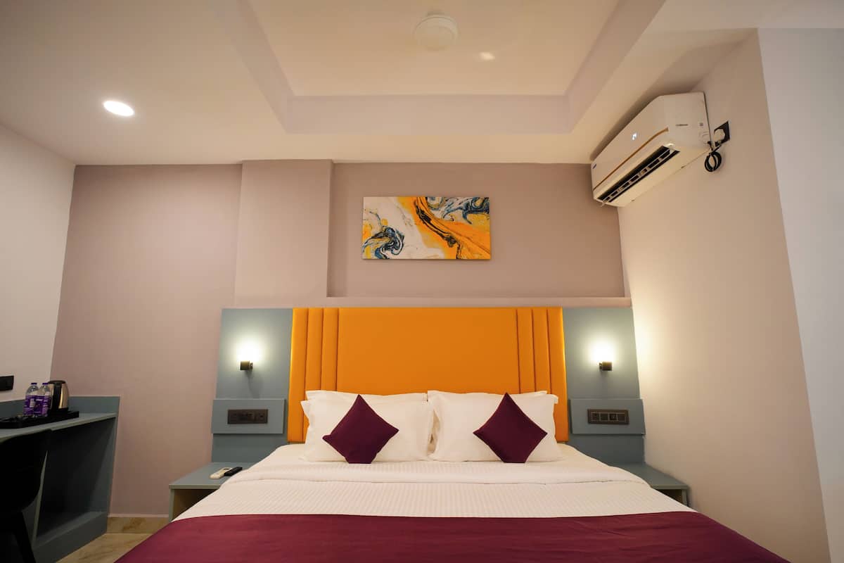 A hotel room with a bed, bedside tables, an air conditioning unit, and a painting on the wall.