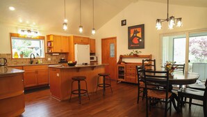 A kitchen with wooden cabinets, a central island with stools, a dining table with chairs, and pendant lighting. - Sauna, River Views, Book Nook, 4BR Homestead Retreat (Stevenson)