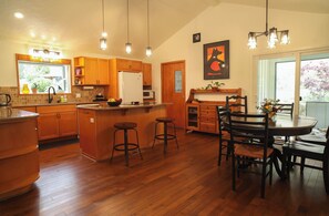 A kitchen with wooden cabinets, a central island with stools, a dining table with chairs, and pendant lighting. - Sauna, River Views, 4BR Homestead Retreat (Stevenson)