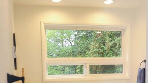 A kitchen with wooden cabinets, a white countertop, a window with a view of trees, and a hanging towel. - Sauna, River Views, Book Nook, 4BR Homestead Retreat (Stevenson)