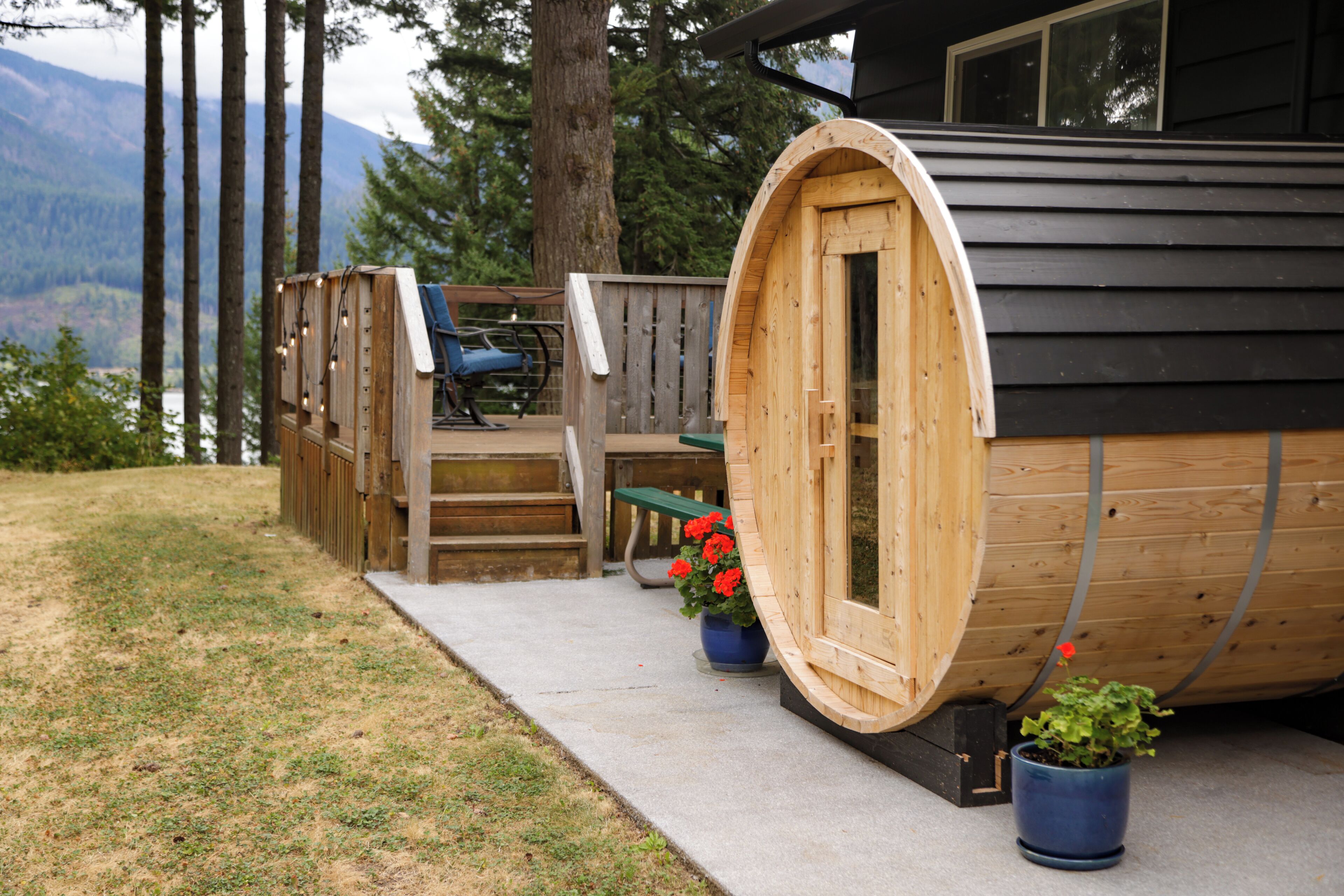 Een houten vakantiehuisje met een grote, trommelvormige deur, een terras met zitplaatsen en potplanten.