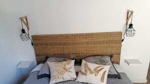 A bed with a woven headboard, two decorative pillows, and two bedside tables with wall-mounted lamps. - Villa 8 persons with private pool (Saint-Florent)