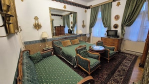 A traditional room with a bed, two armchairs, a small table, a dresser, a mirror, and a television. - Imre Guest House (Budapest)