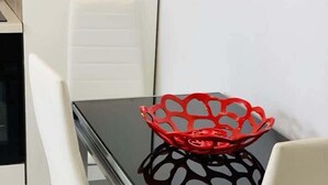 Een eettafel met een zwarte glazen blad en een rode decoratieve schaal.
