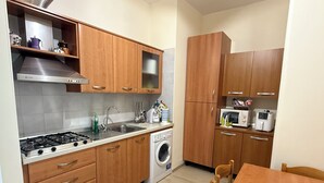 A compact kitchen with wooden cabinets, a gas stove, a microwave, and a washing machine. - Welcoming and well-kept, it is the perfect base for discovering the wonders of Salento. (Lizzanello)