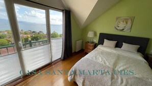 A bedroom with a large window, a bed with white bedding, a nightstand, and a wall-mounted lamp. - Casa Santa Marta Cies - Your perfect refuge with views of the Islas Cíes (Cangas)