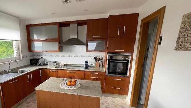 A kitchen with wooden cabinets, a countertop, a sink, a stove, and a window. - Casa Santa Marta Cies - Your perfect refuge with views of the Islas Cíes (Cangas)
