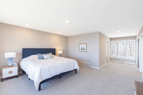 Une chambre à coucher avec un grand lit, des tables de chevet, une fenêtre et un tableau encadré au mur.