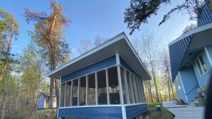 A modern house with a large covered porch, surrounded by trees.