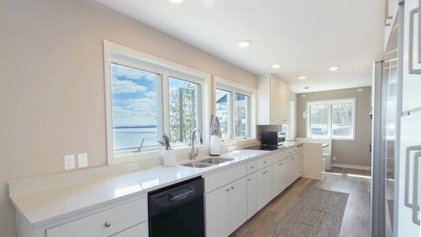 A modern kitchen with a dishwasher, a sink, and a large window overlooking a body of water.