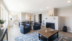 A spacious living room with a fireplace, a dining area, and a kitchen in the background.