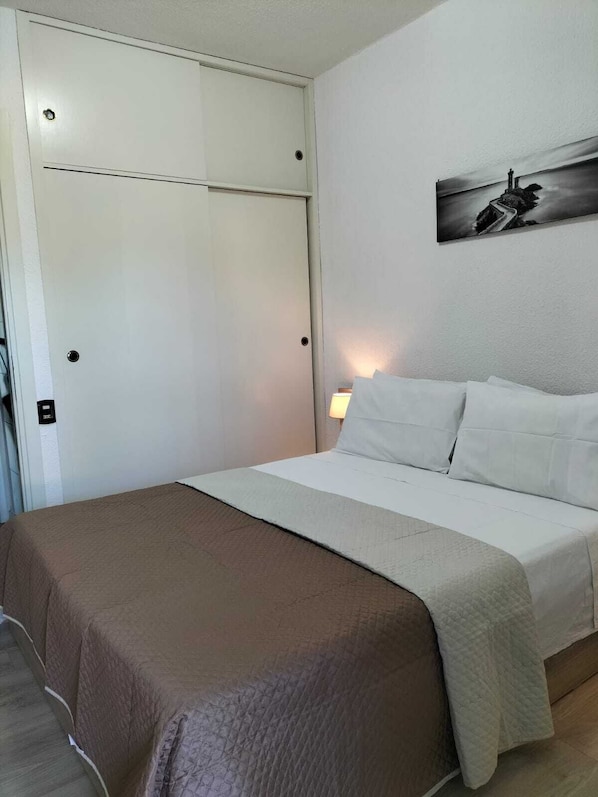 A hotel room with a bed, a nightstand, a wall-mounted painting, and a door with a handle.