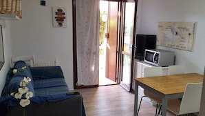 A compact living space with a bed, a small table, a microwave, and a television.