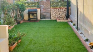 A backyard with artificial grass, a barbecue grill, and a stone wall.
