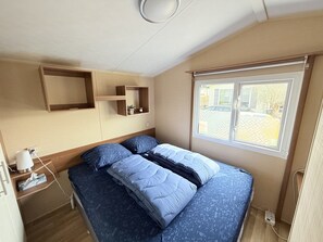 A bedroom with a bed, a bedside table with a lamp, a small shelf, and a window with a view of the outside. - RBR 644 - Beach Resort Kamperland (Kamperland)