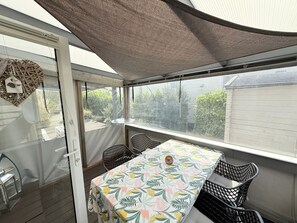 A covered patio area with a table and chairs, a view of greenery outside, and a door with a woven shade. - RBR 644 - Beach Resort Kamperland (Kamperland)